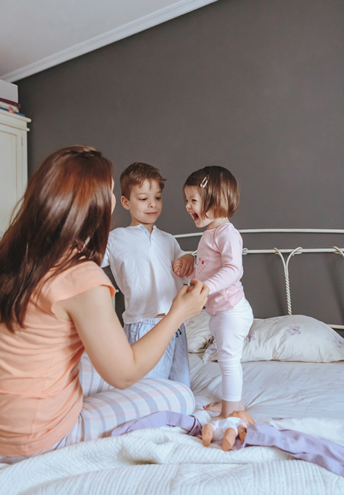 Relaxed mother and sons playing over the bed